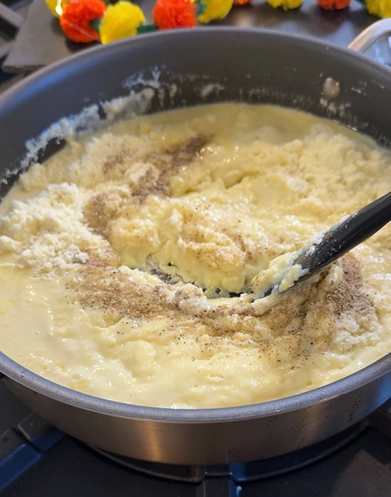 a spatula stirring milk powder in a pan with cardamom powder