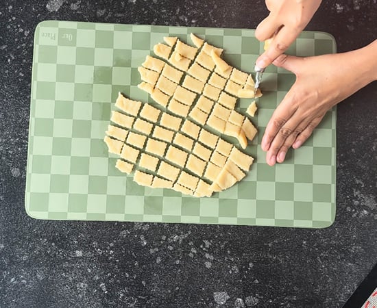 dough being cut using a pastry cutter into square shape