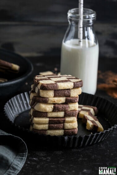 stack of checkerboard cookies with a bottle of milk in the background