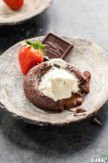 eggless chocolate lava cake served on a plate topped with ice cream and a strawberry and chocolate piece placed on the side