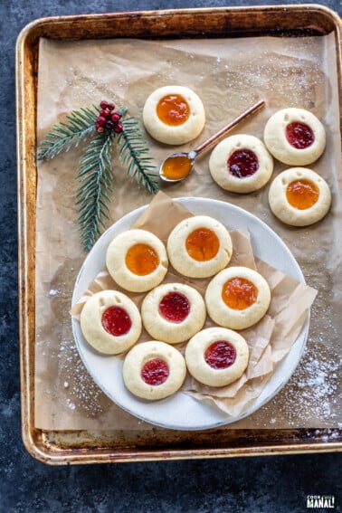 thumbprint cookies arranged on a white plate with more cookies placed in the background