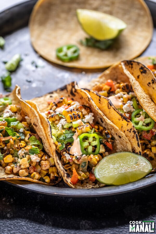 grilled corn tacos arranged on a plate with a lime wedge placed on the side