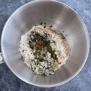 a steel bowl with flour, fenugreek leaves, spices