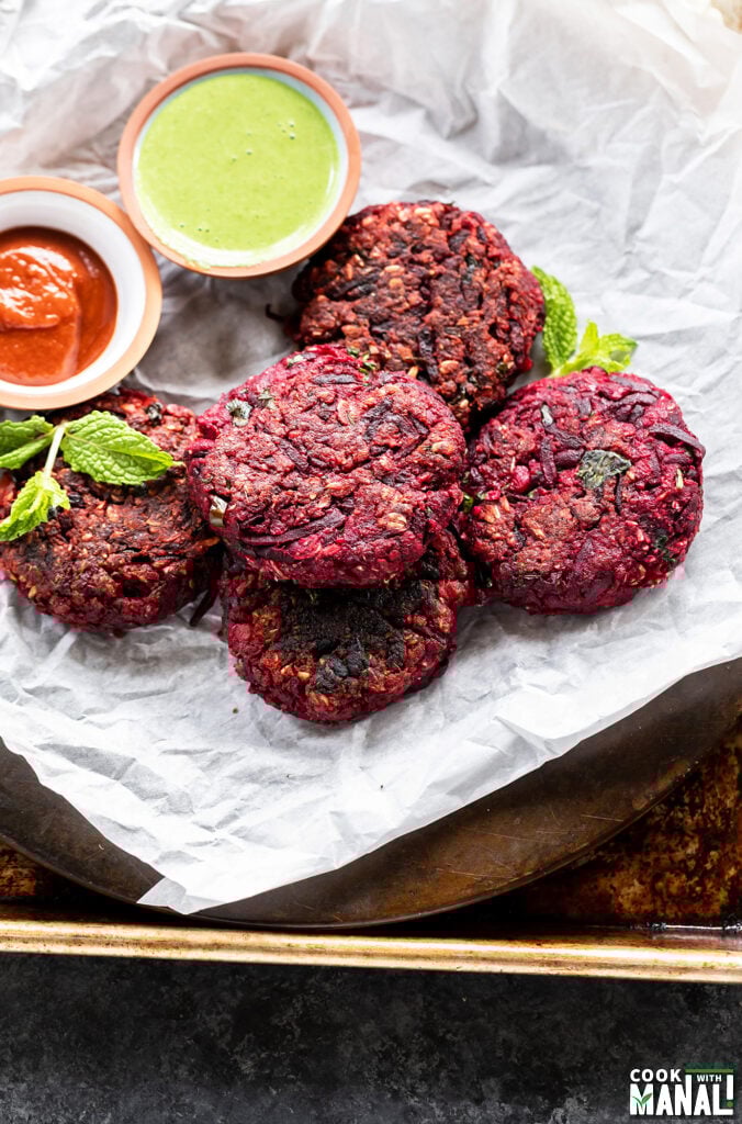 tikkis arranged on a plate with bowls of chutney and ketchup on the side