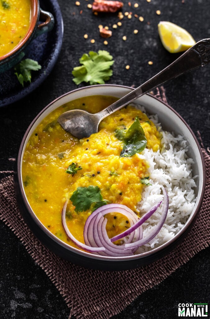 bowl of moong dal tadka and rice served with sliced onions