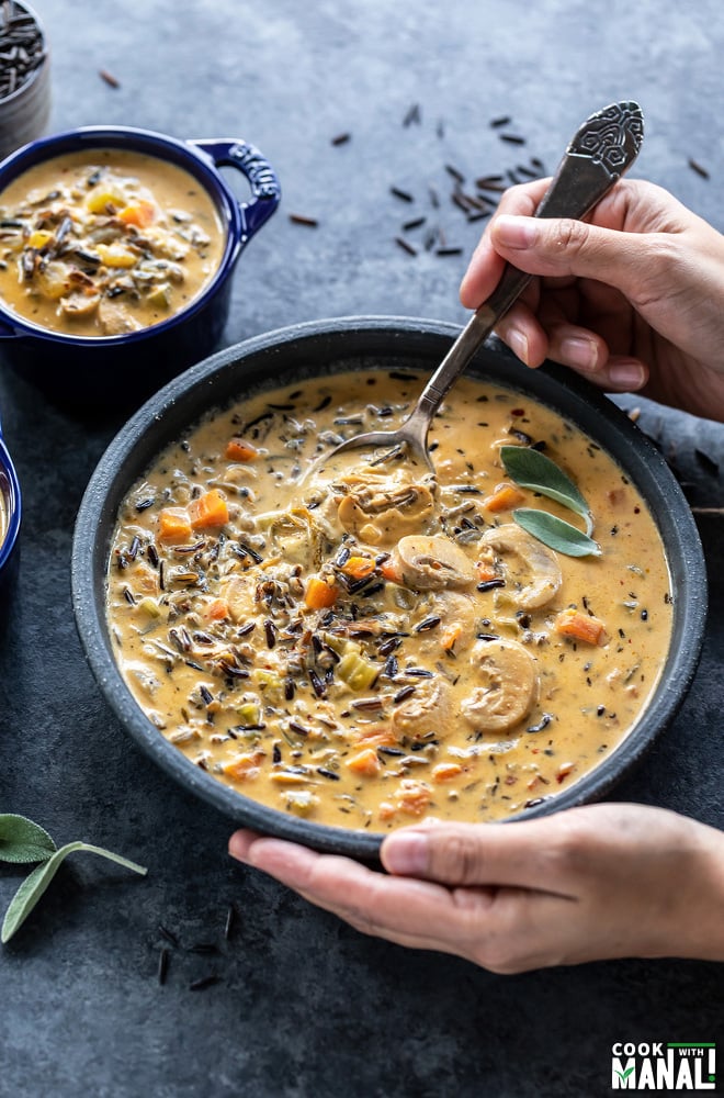 a pair of hands digging into a bowl of mushroom wild rice soup with a spoon