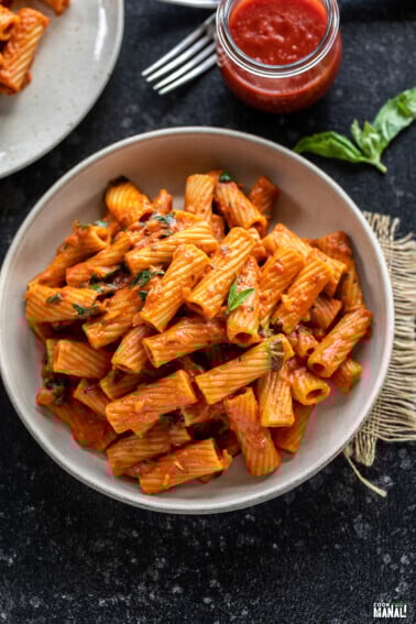 rigatoni pasta served in a white round bowl, garnished with basil
