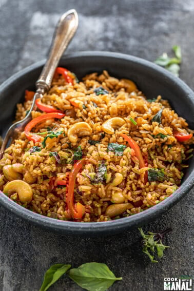 thai basil fried rice in a black bowl with a fork and few basil leaves scattered around