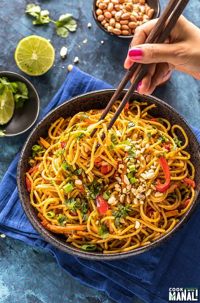 thai peanut noodles in a black bowl with a hand holding chopsticks