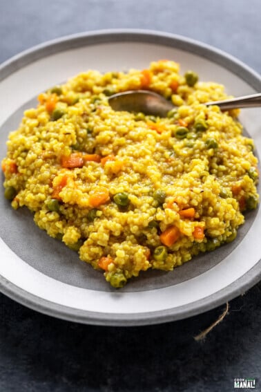vegetable daliya served on a white plate with spoon on the side