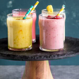 four glasses of lassi with straw on a cake stand
