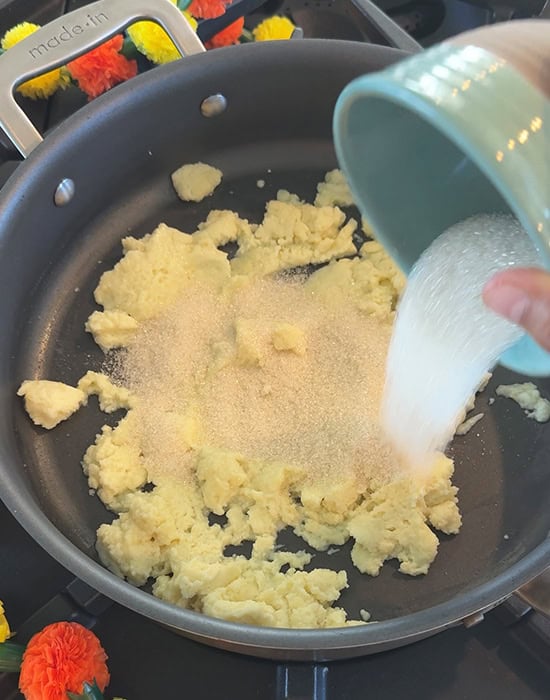 a bowl of sugar being added to mawa in a pan