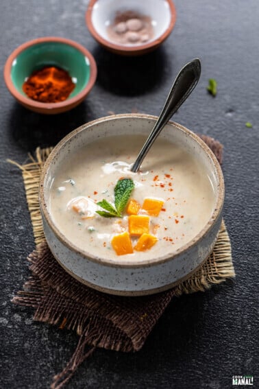 raita served in a white bowl topped with mango and garnished with mint