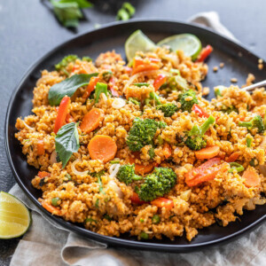 black plate with quinoa, veggies, basil, lime wedge and more basil and a bowl of hot sauce in the background