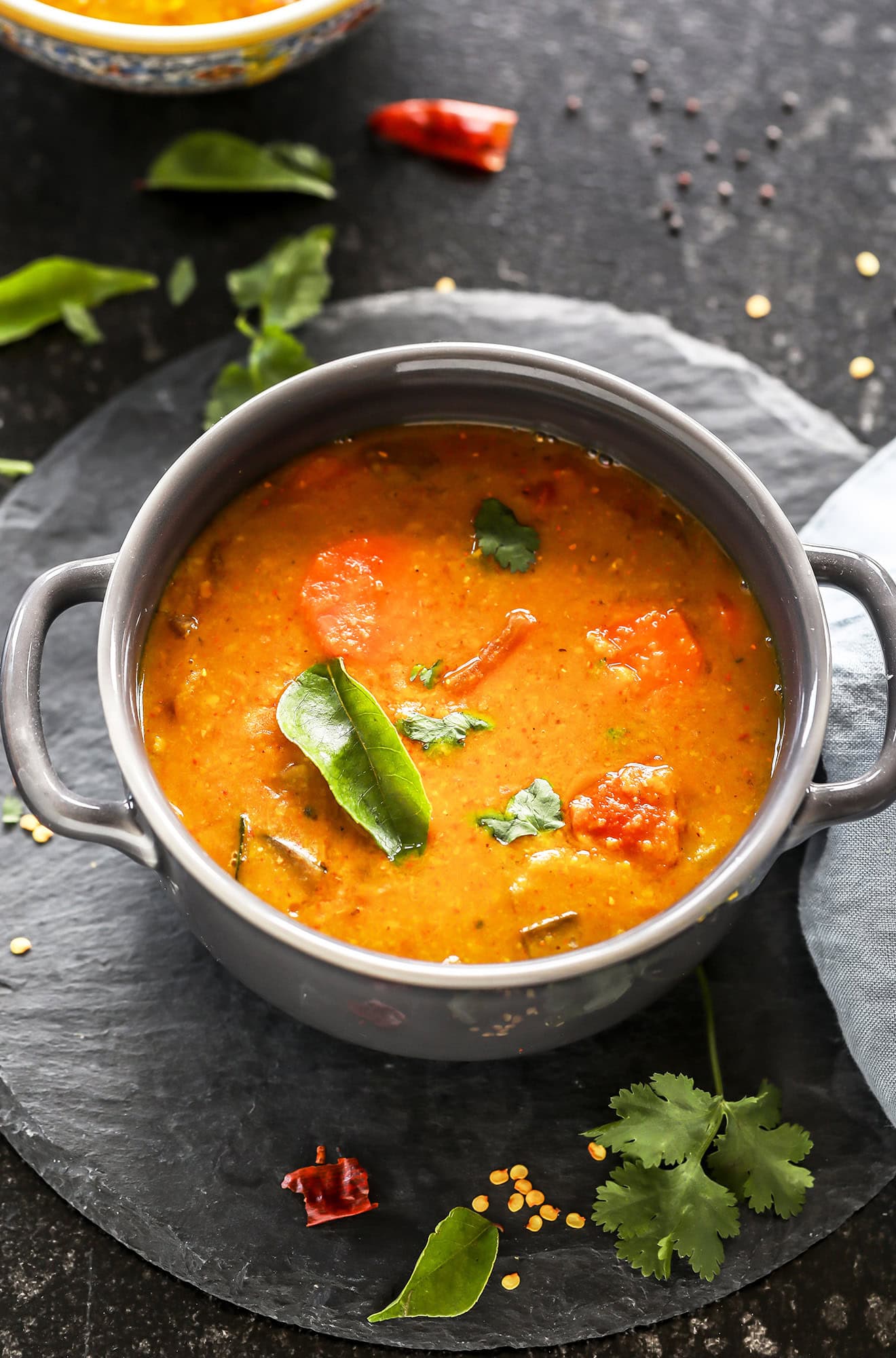 sambar served in a grey bowl garnished with curry leaves with twigs on cilantro and more curry leaves scattered all around