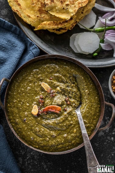 sarson ka saag served in a iron kadhai with makki roti and sliced radish and green chilies