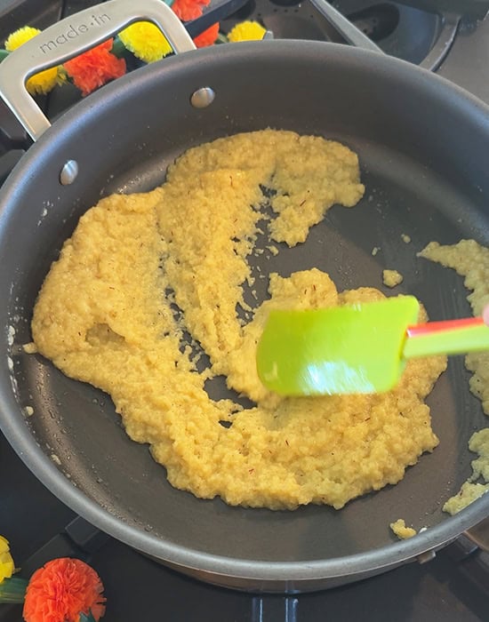 a green color spatula stirring mawa in a pan