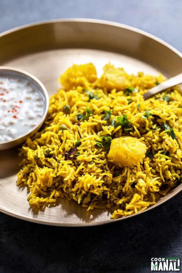 tehri served in a brass plate with a bowl of yogurt on side