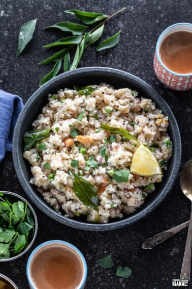 bowl of upma with glass of chai on one side, blue color kitchen towel on another side and curry leaves in the background